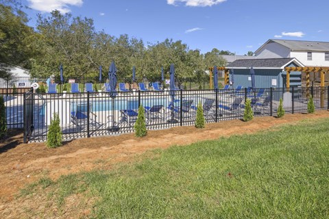 A pool surrounded by a black fence with blue lounge chairs and trees in the background.