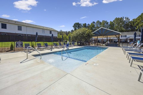 A large outdoor swimming pool surrounded by lounge chairs and a building in the background.