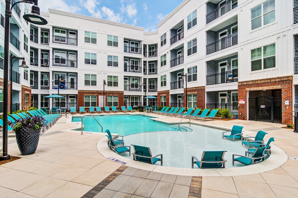 an empty swimming pool with blue chairs in front of an apartment building