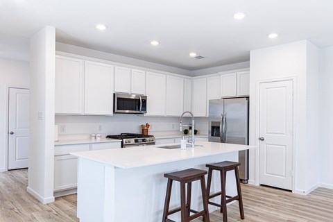 A kitchen with white cabinets and a white island with two stools.