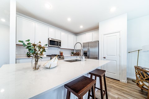 A kitchen with a white counter top and a wooden stool.