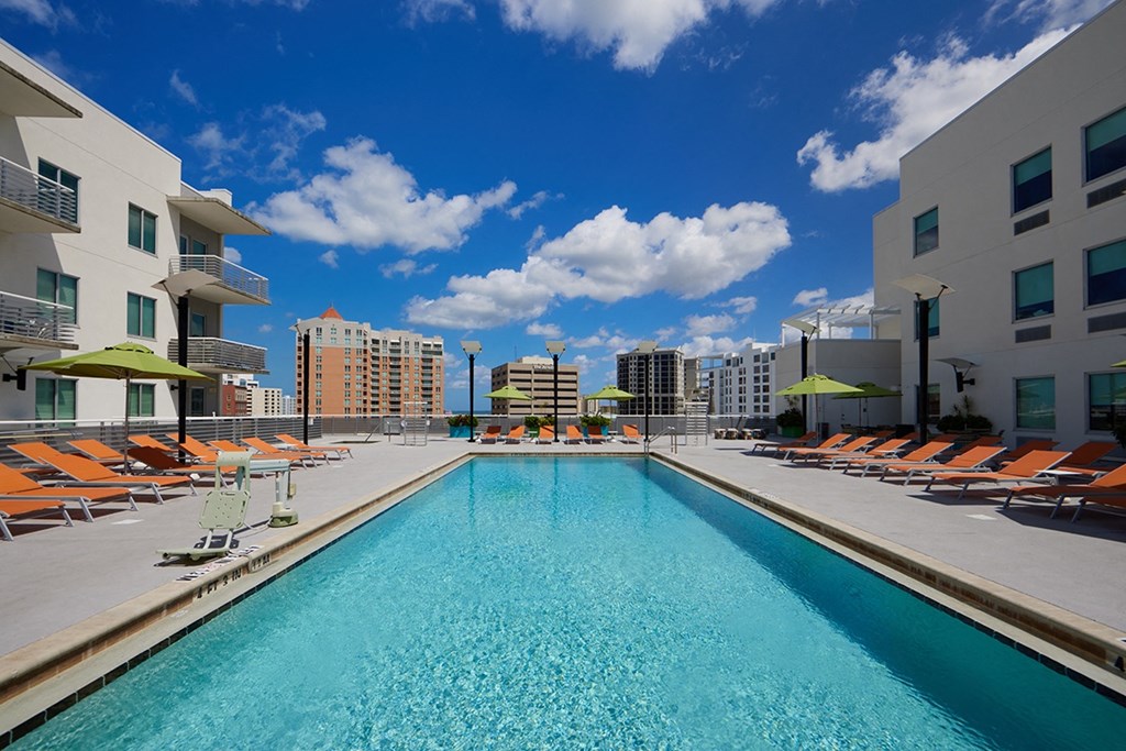 a swimming pool with orange lounge chairs and buildings in the background