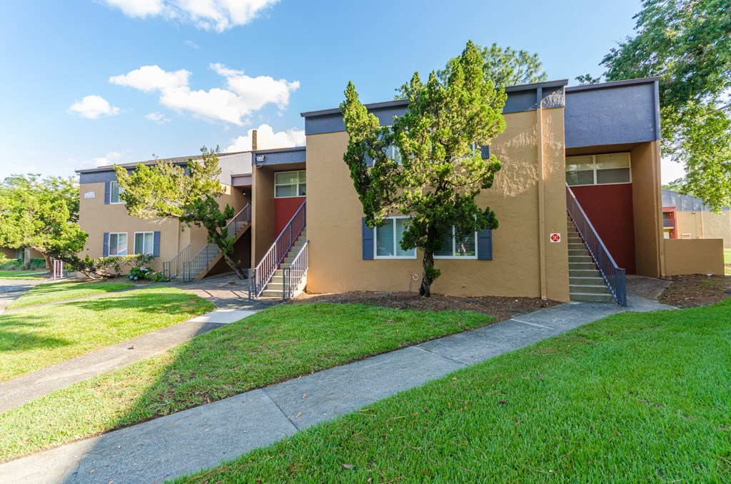 an exterior view of a yellow building with stairs and grass and trees