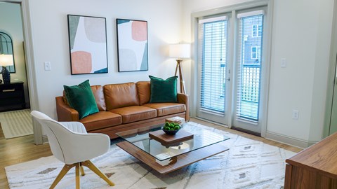 A living room with a brown leather couch, a white chair, and two abstract paintings on the wall.