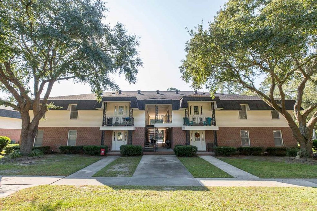 A two-story apartment building with a front lawn and trees.