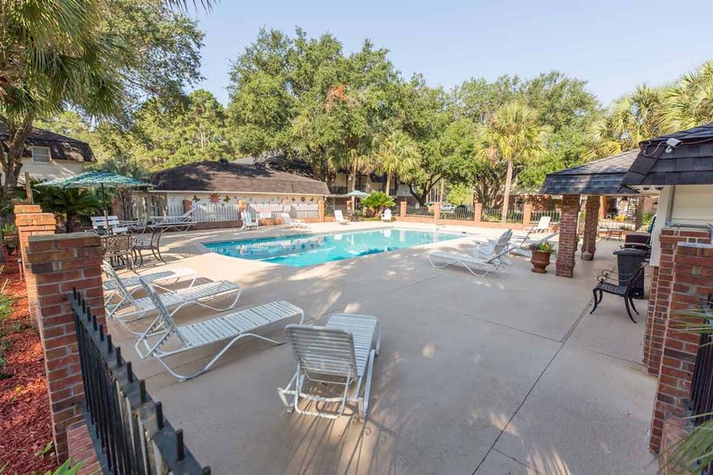 A pool surrounded by a patio with chairs and umbrellas.