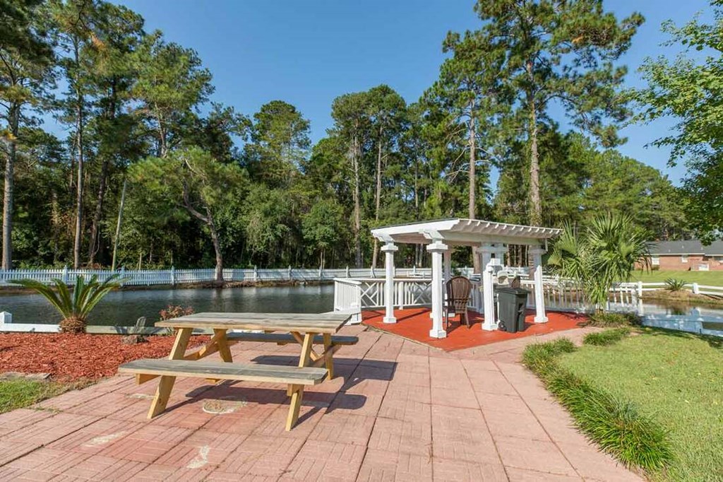 A pavilion with picnic tables is surrounded by trees and a body of water.