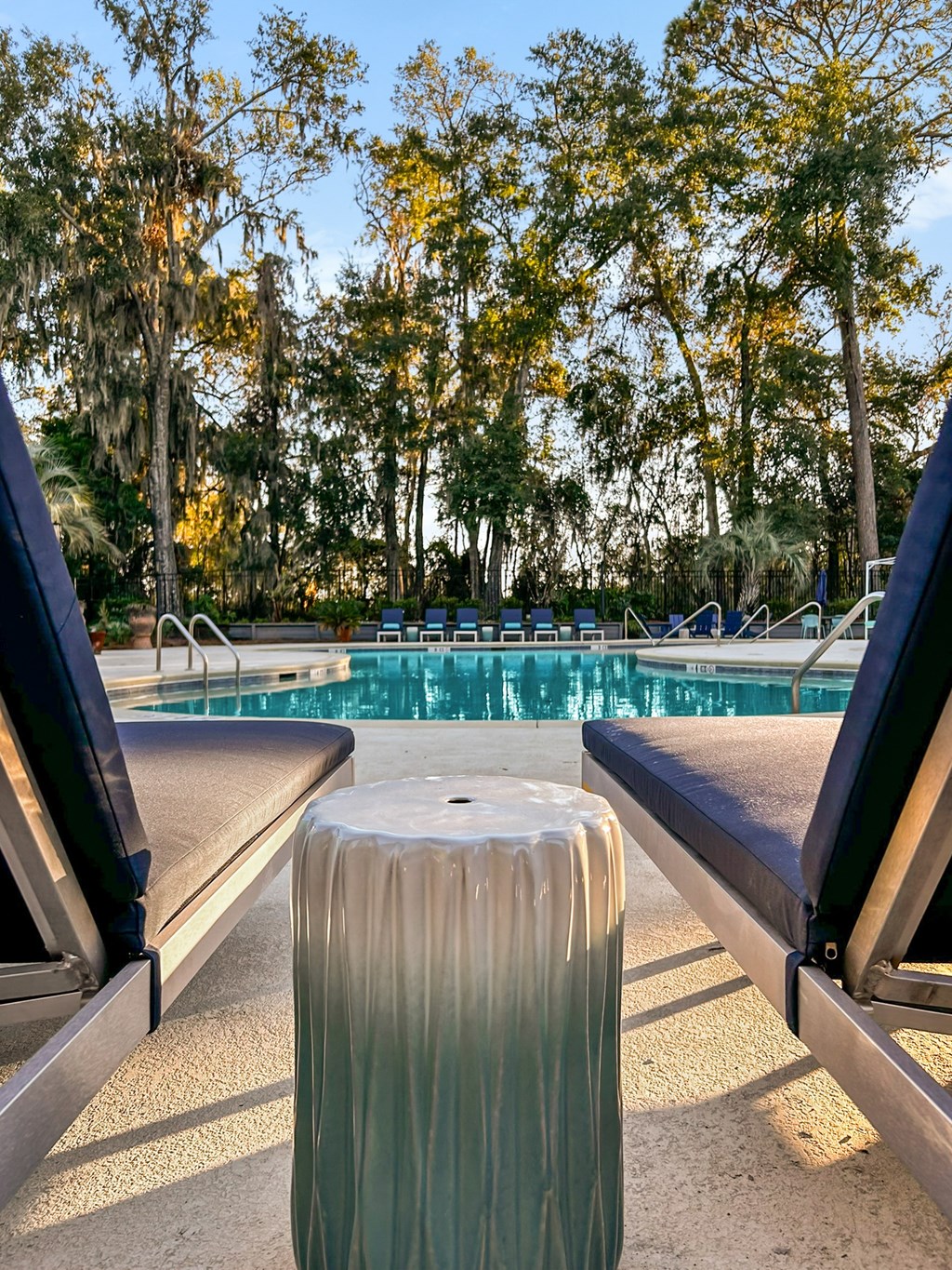 A pool with sun loungers and a tree in the background.