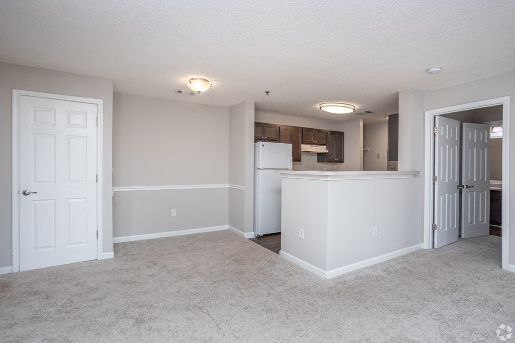 an empty living room and kitchen with a refrigerator and a sink
