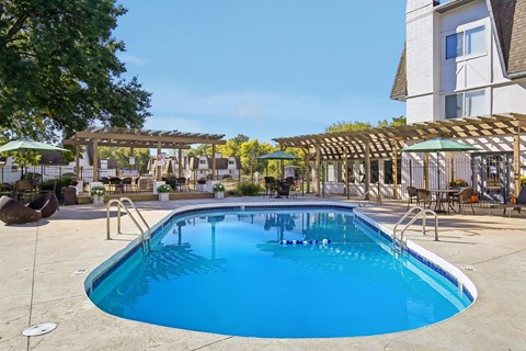 A large outdoor swimming pool with a wooden pergola and lounge chairs.