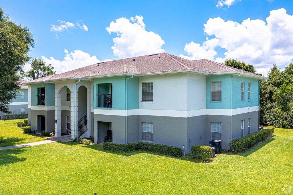 a white and blue house with a green lawn and trees at Waters Edge Apartments, Lakeland