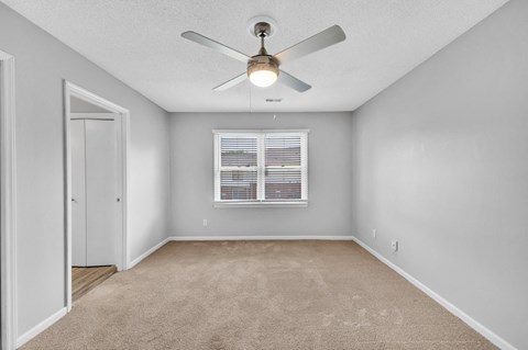 an empty bedroom with a window and ceiling fan