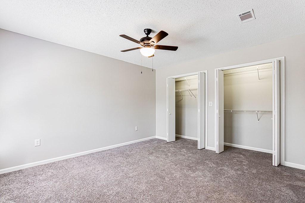 an empty bedroom with a ceiling fan and closet
