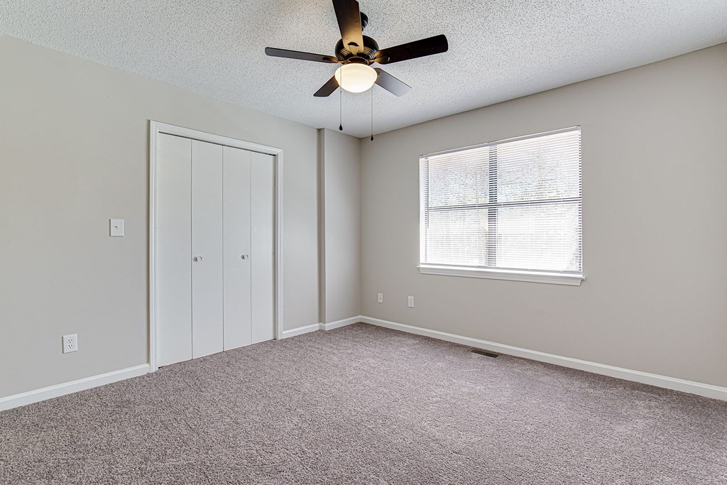 an empty living room with a ceiling fan and a closet