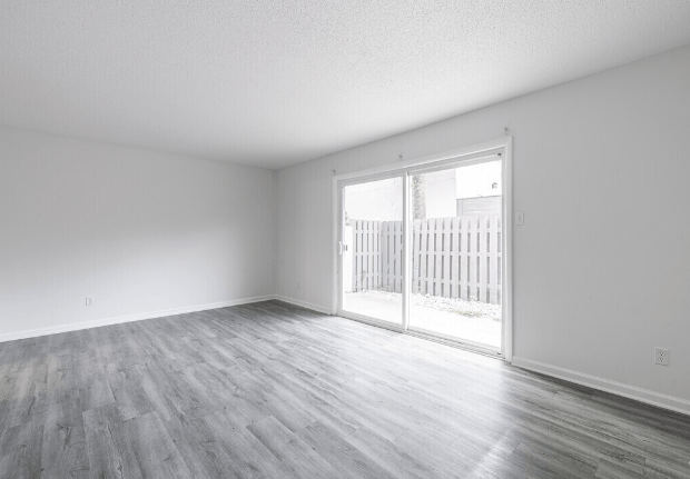 an empty living room with wood floors and a sliding glass door at Crescent Place Apartments, Savannah, GA