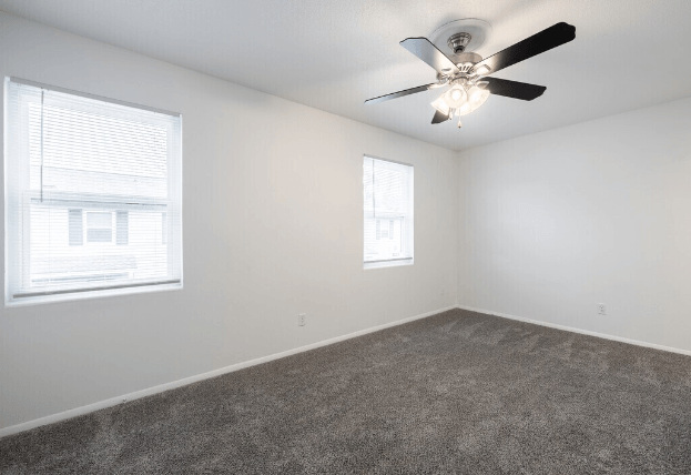 an empty living room with a ceiling fan and two windows at Crescent Place Apartments, Savannah, 31419