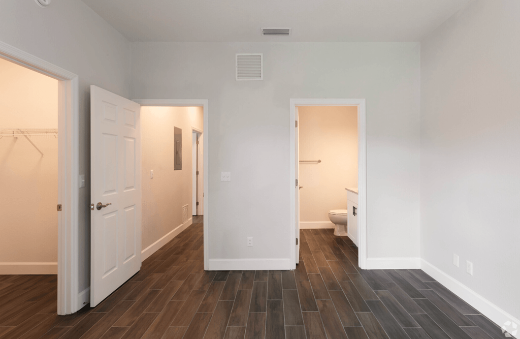 a bedroom with a door to a bathroom and a closetan empty room with a large window and wood flooring
