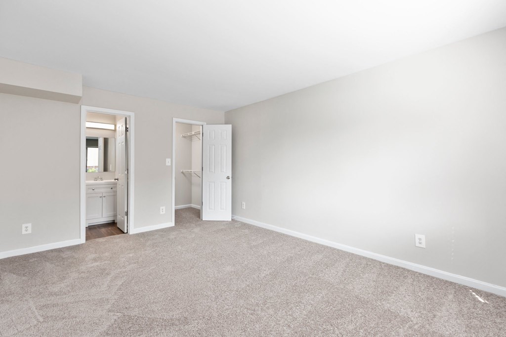 a bedroom with a carpeted floor and a bathroom in the background