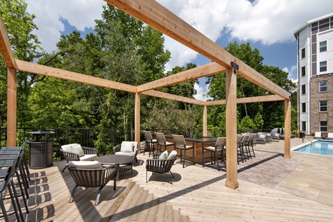 A wooden pergola over a patio with chairs and a table.