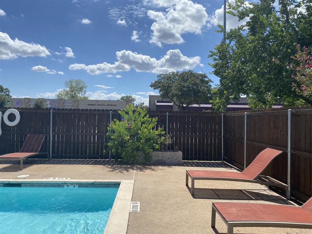 a backyard with a pool and two lounge chairs     and a fence