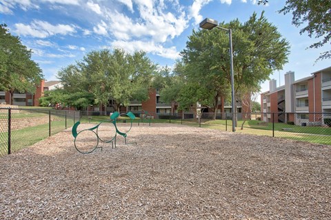 A playground with a green swing set and a brown gravel ground.