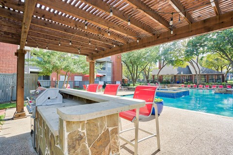 A poolside bar area with a stone counter and red chairs.