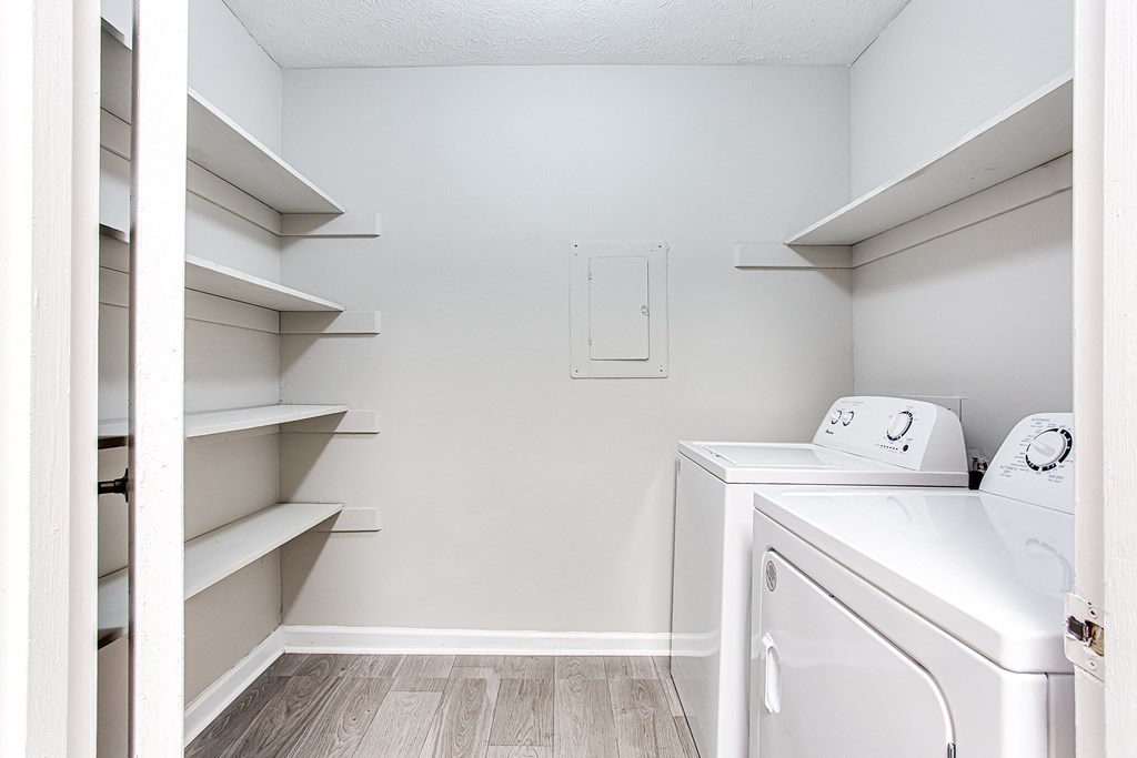 a washer and dryer in a white laundry room with shelves at The Ellis Apartments, Clarkston, GA