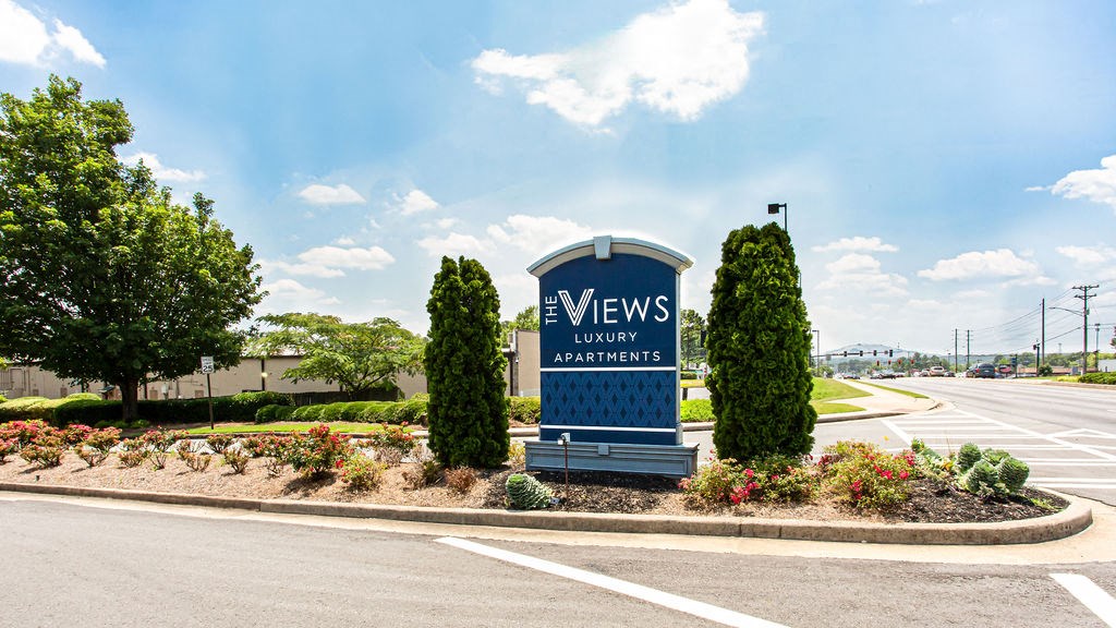 a blue sign with white writing and a blue bench in front of a parking lot