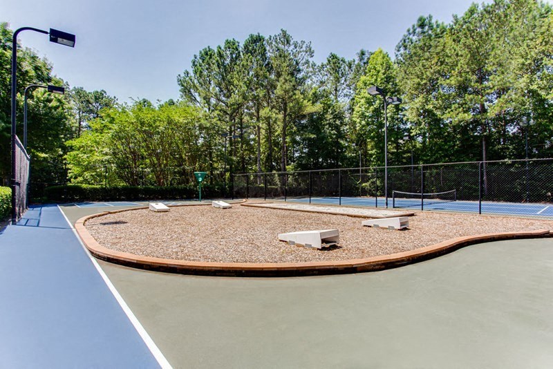 a tennis court with two benches on it and trees in the background