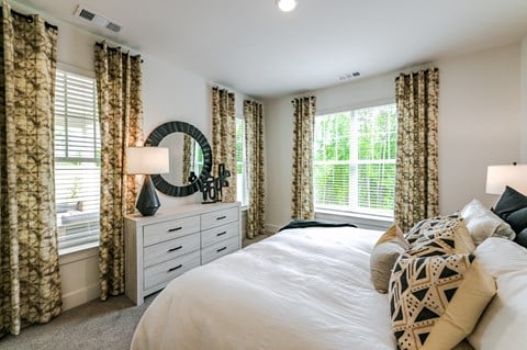 A bedroom with a large bed, a dresser with a mirror, and patterned curtains.
