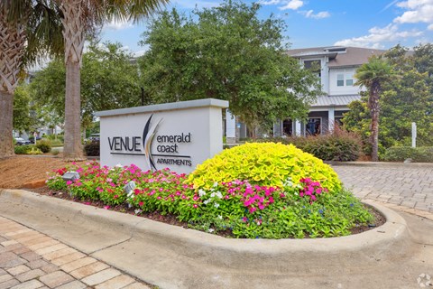 A sign for Venice Emerald Coast Apartments is surrounded by flowers.