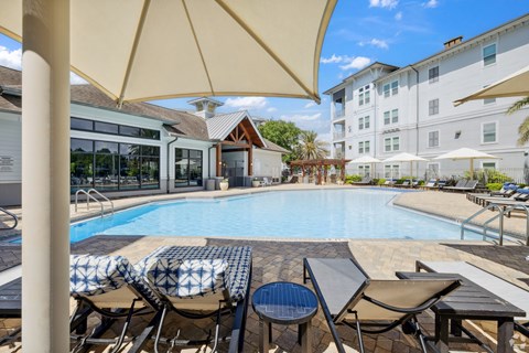 A pool area with chairs and umbrellas is surrounded by apartment buildings.