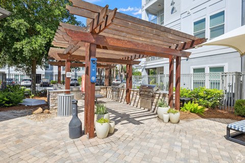 A wooden pergola with a blue sign on it is in the middle of a brick patio.