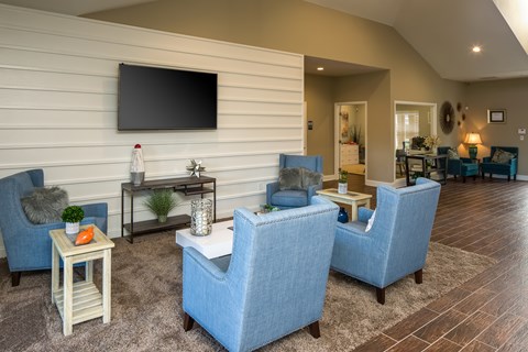 A living room with blue chairs and a flat screen TV mounted on the wall.