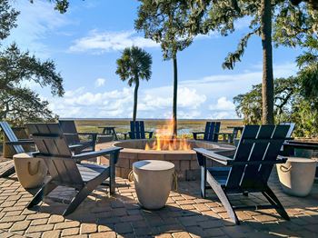 A fire pit sits in the middle of a patio surrounded by chairs.
