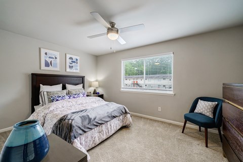 A bedroom with a bed, chair, and ceiling fan.