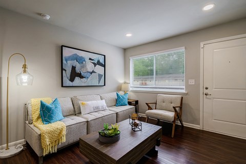 A living room with a grey couch, a yellow throw blanket, a coffee table, and a painting on the wall.