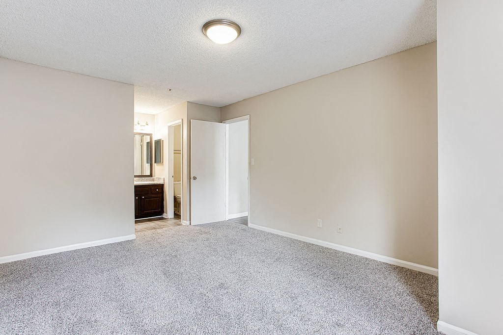 an empty living room with white carpet and a door to a bathroom