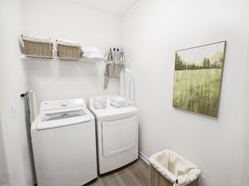 A laundry room with a washer and dryer, a basket, and a painting on the wall.