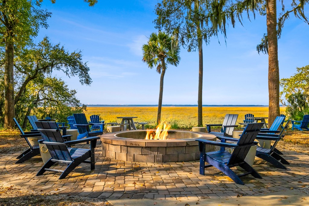 A fire pit surrounded by blue chairs and palm trees.