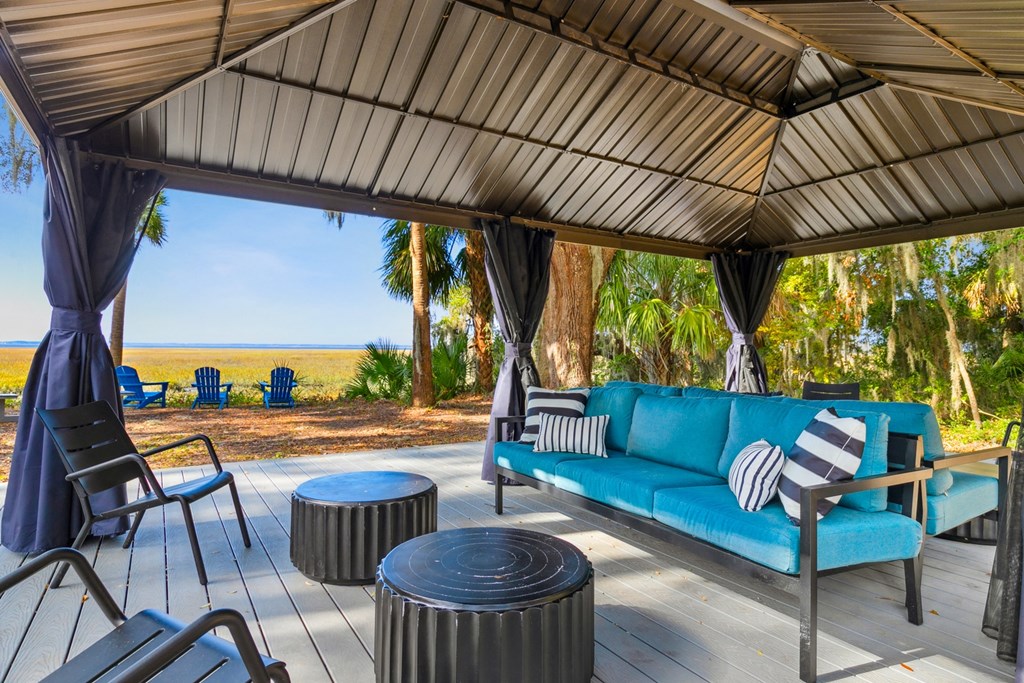 A blue couch with striped pillows sits under a canopy on a wooden deck.