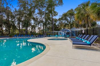 A pool surrounded by trees and lounge chairs.