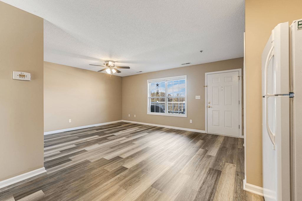 an empty living room with a white door and a ceiling fan