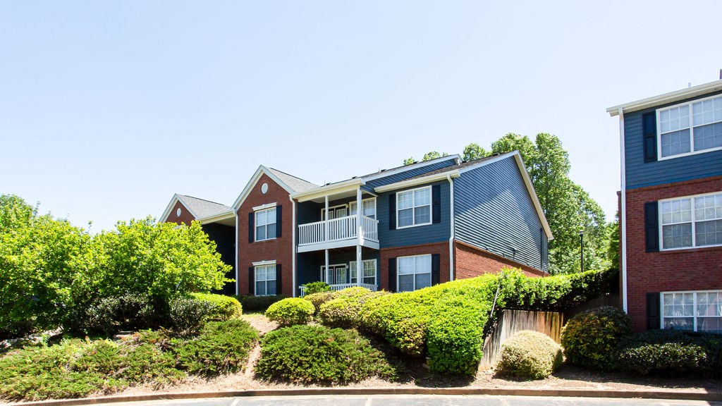 a brick apartment building with a blue roof and green shrubbery in front of it