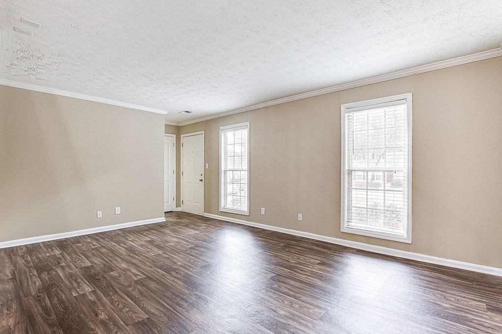 an empty living room with wood floors and a door to a hallway