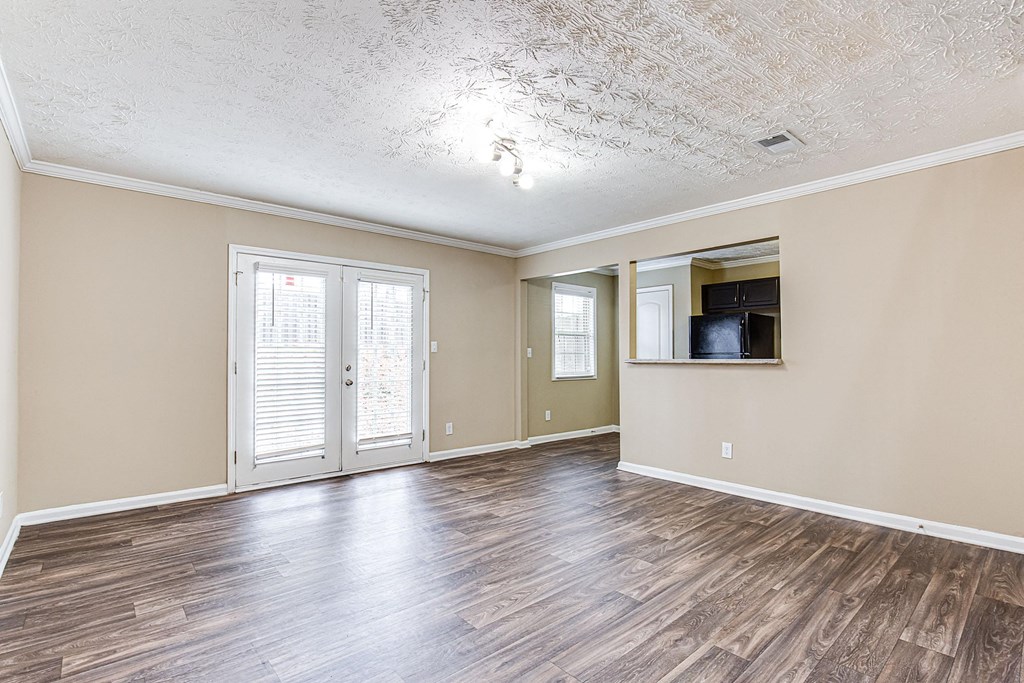 an empty living room with a door to the kitchen and a window