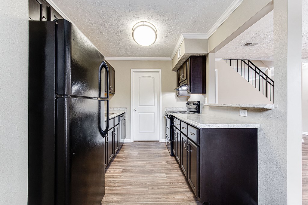 an empty kitchen with black appliances and a white staircase