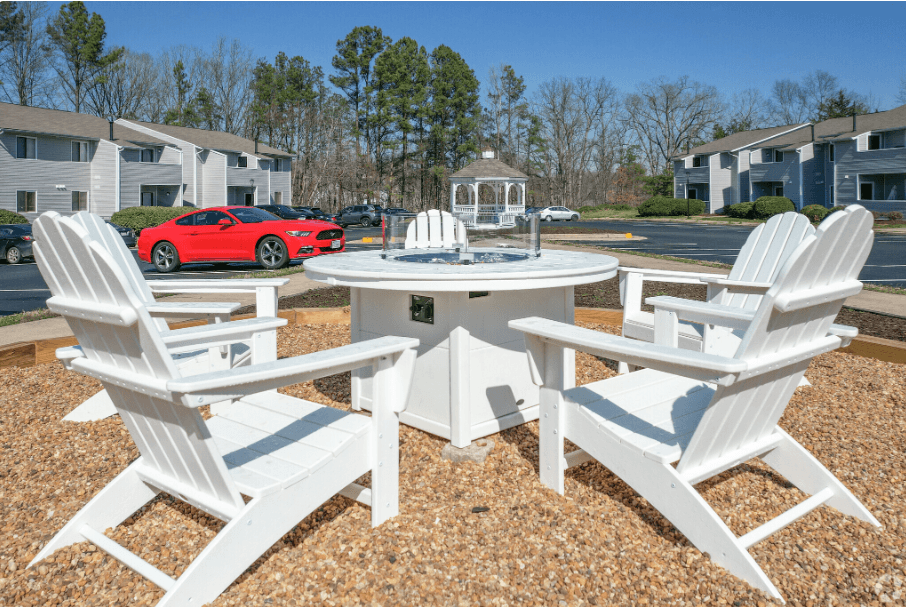 a patio with a table and chairs and a red car parked in a parking lot