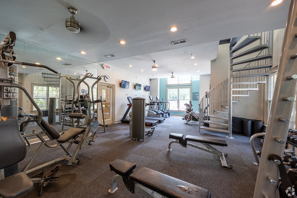 a gym with weights and cardio equipment and a spiral staircase  at Flats at North Springs, Sandy Springs, GA, 30328