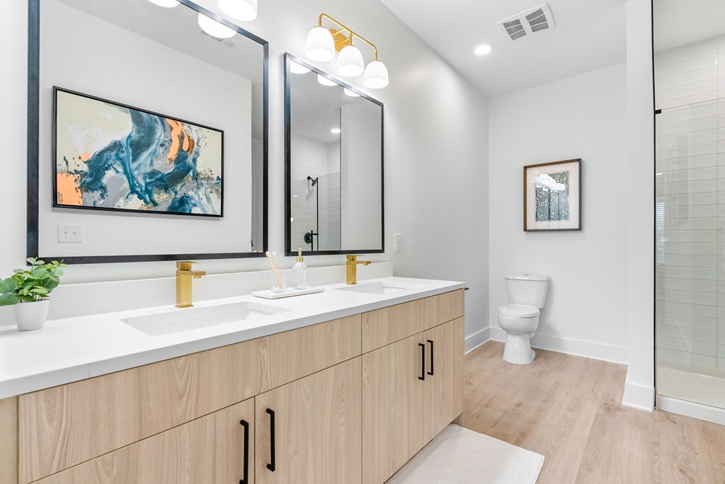 A bathroom with a large mirror, a sink, a toilet, and a plant.
